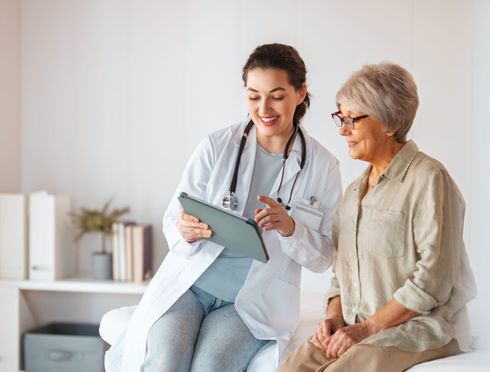 A doctor is standing next to an elderly woman in a wheelchair.