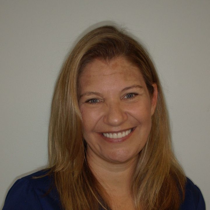 Woman with long blonde hair, smiling broadly, wearing a blue shirt.
