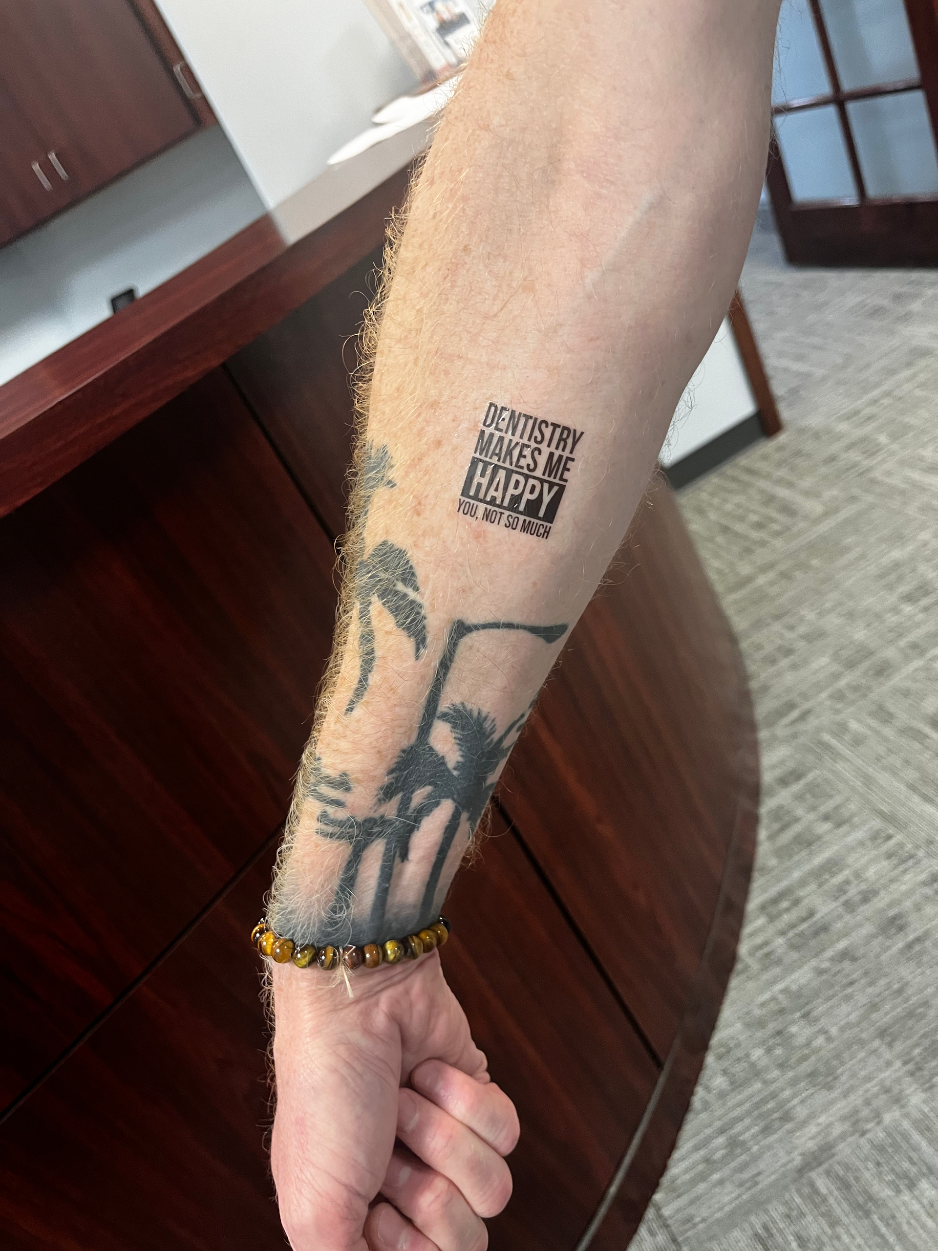 Arm with two tattoos: a QR code and palm trees, wrist with a beaded bracelet.