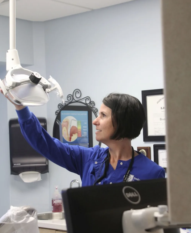 A woman in a blue shirt is looking up at a dental light