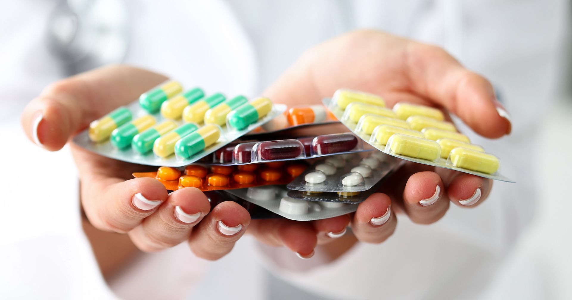 A person is holding a pile of pills in their hands.