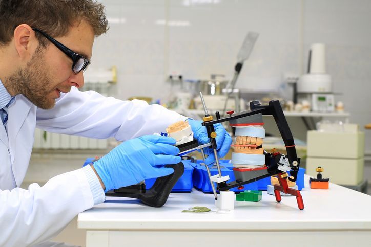 Dentist in lab coat and gloves adjusts dental model on a device.