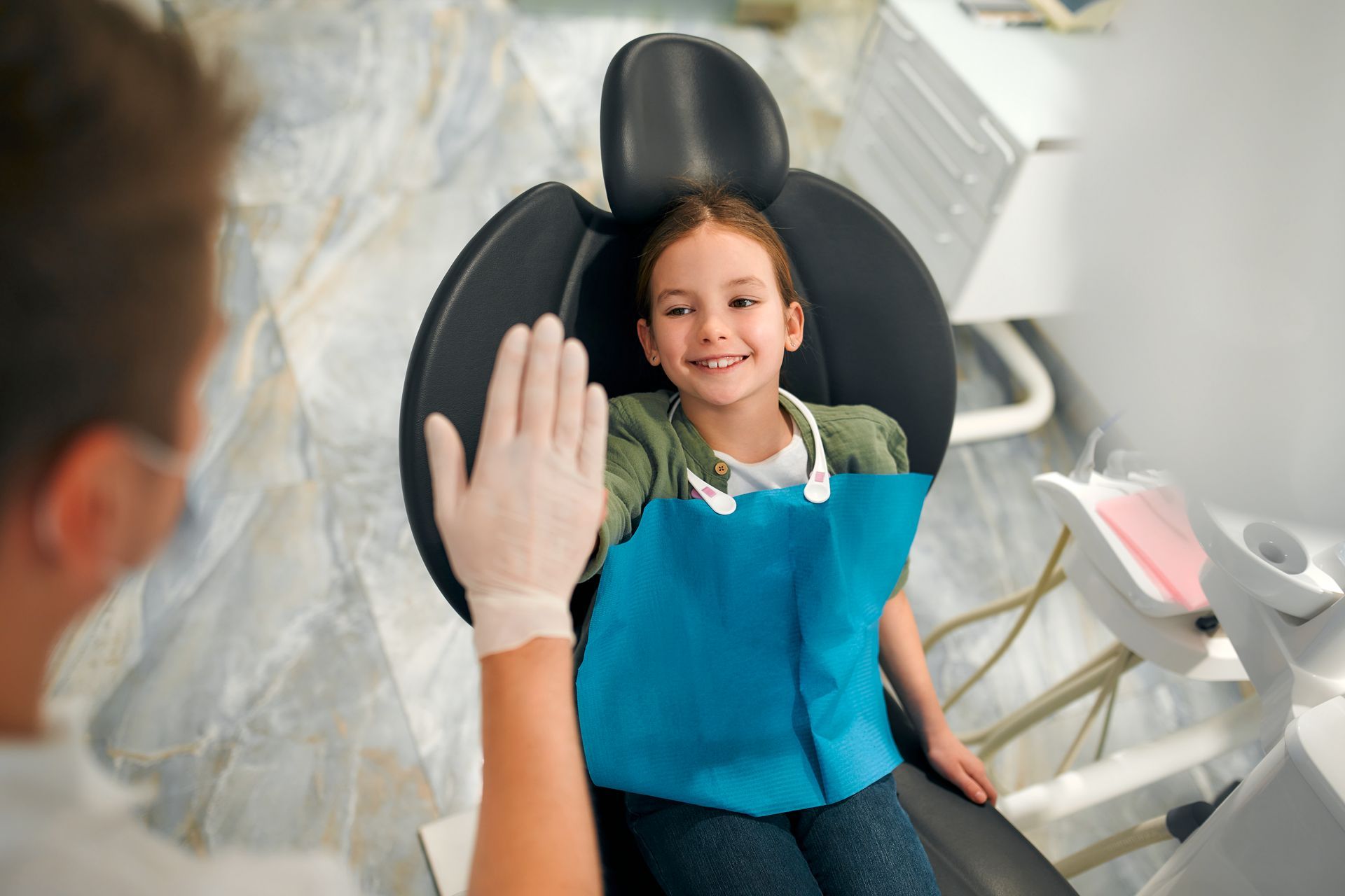 A little girl is sitting in a dental chair giving the dentist a high five.
