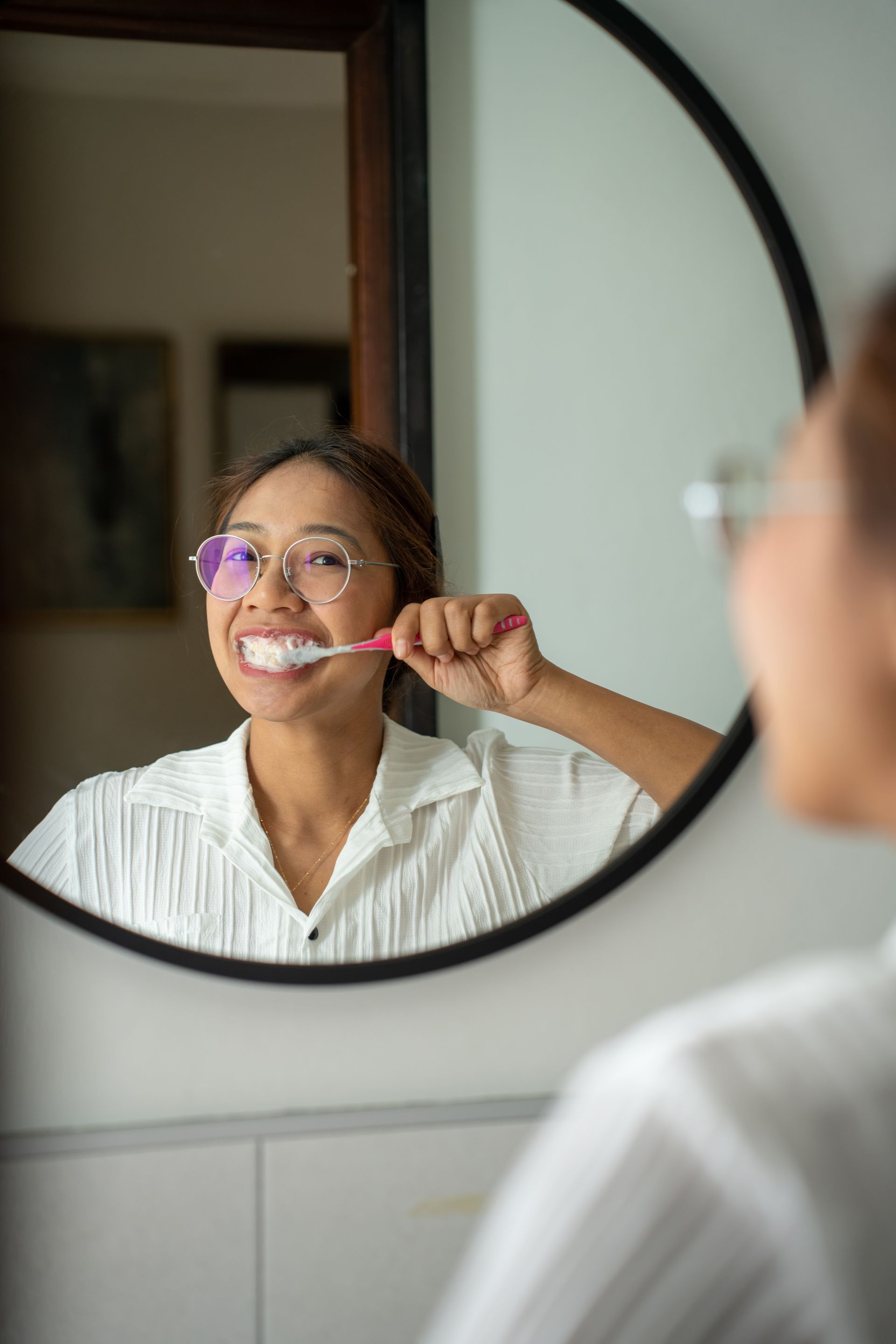 A woman is brushing her teeth in front of a mirror.