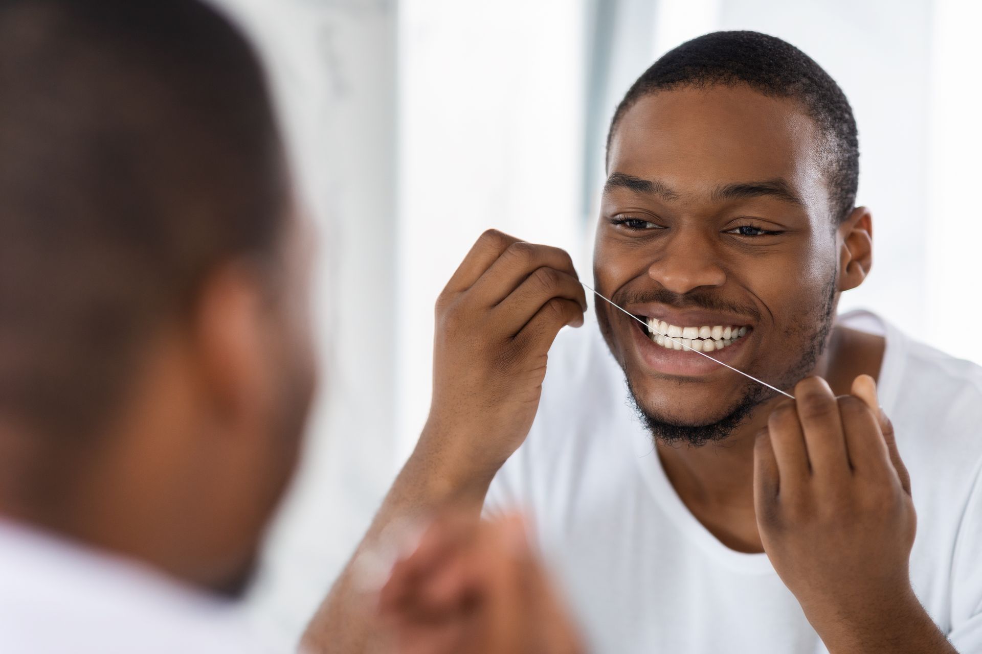 A man is flossing his teeth in front of a mirror.