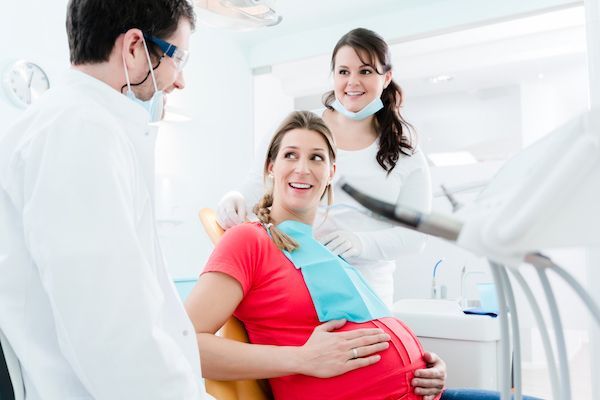 A pregnant woman is sitting in a dental chair talking to a dentist.