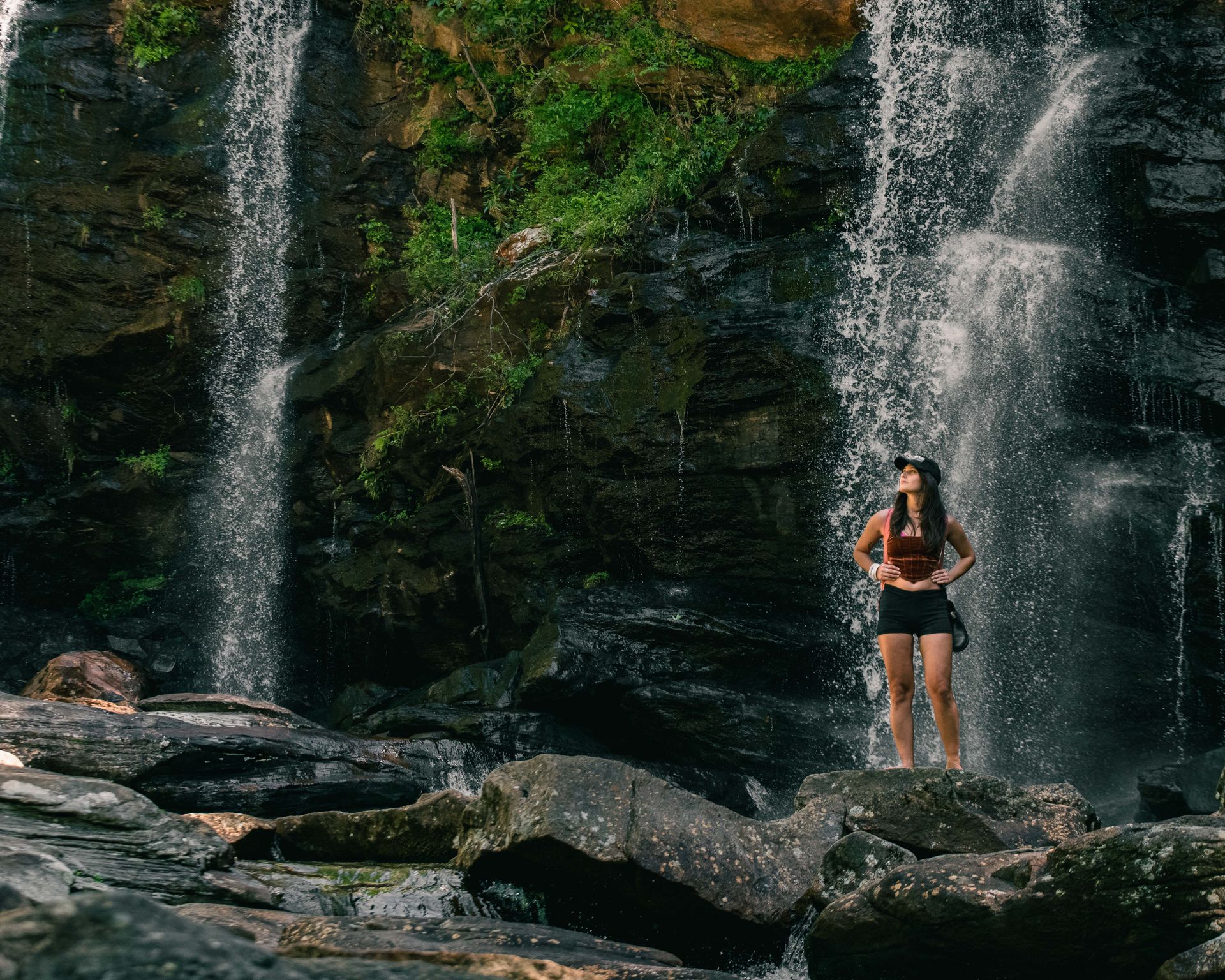 A woman stands in front of a waterfall.
