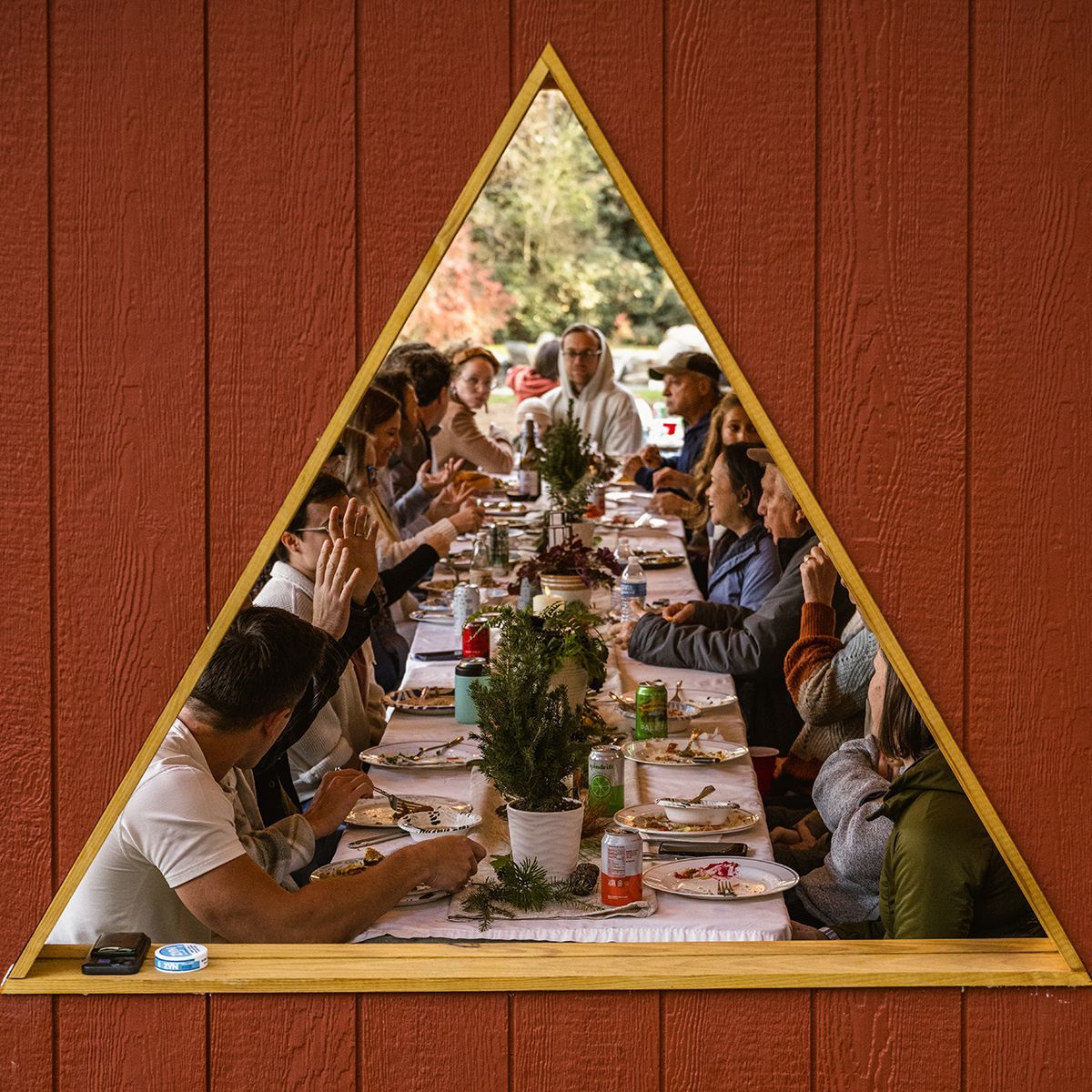 People eat at a long table seen through a triangle window.