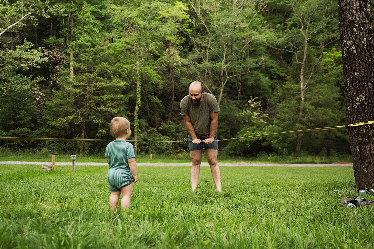 A baby and a man hang out near a slackline.