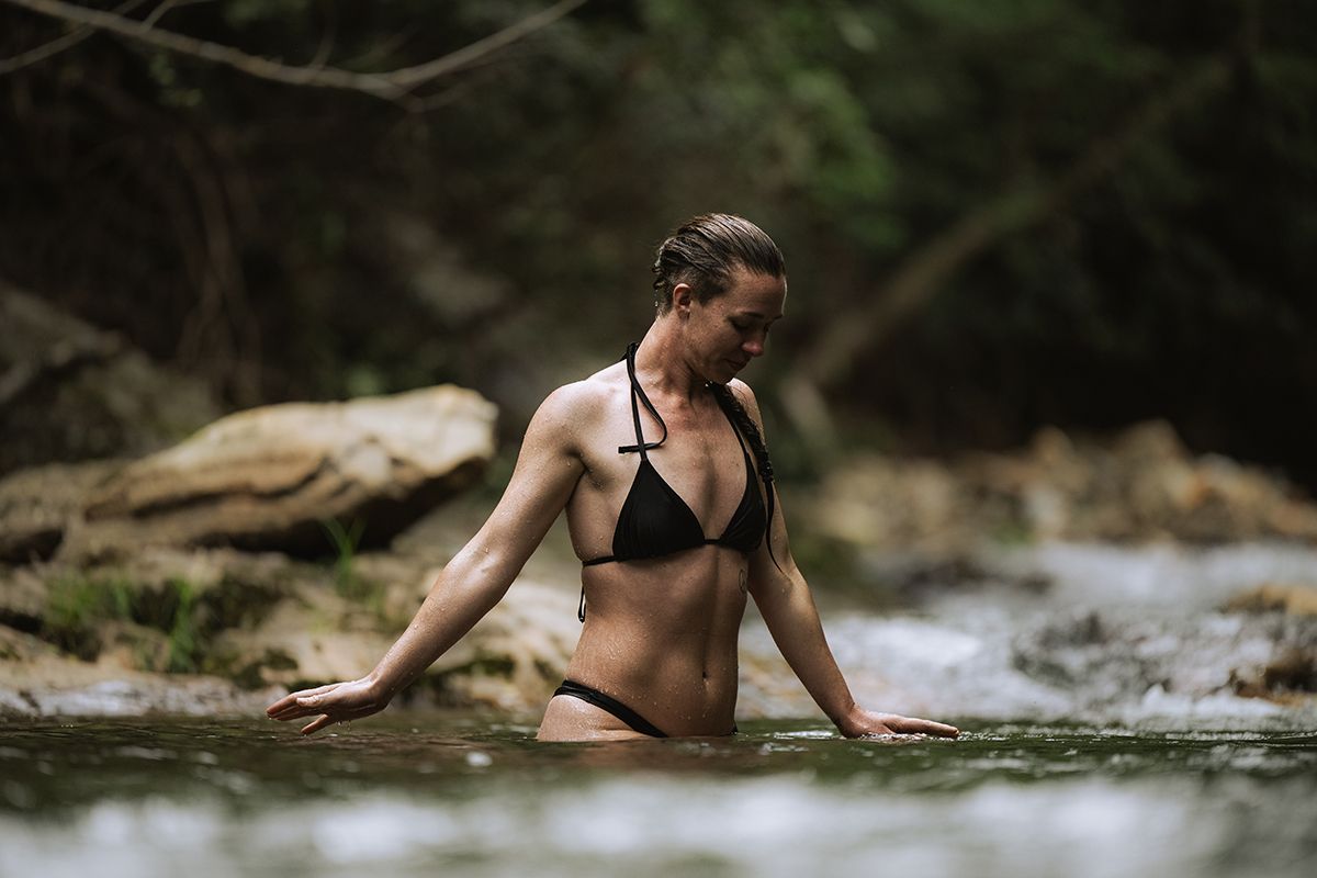 A woman cold plunges in a natural river.