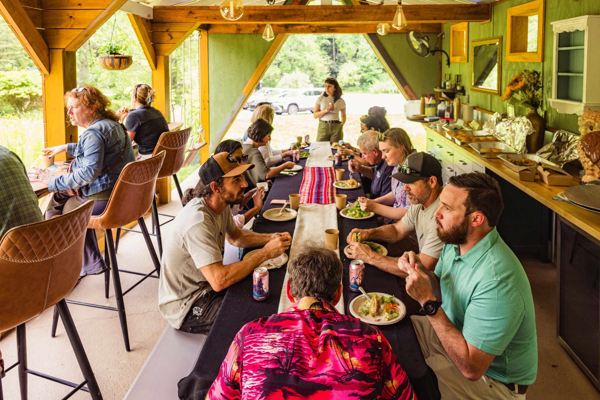 People gather at a long table in an outdoor kitchen.