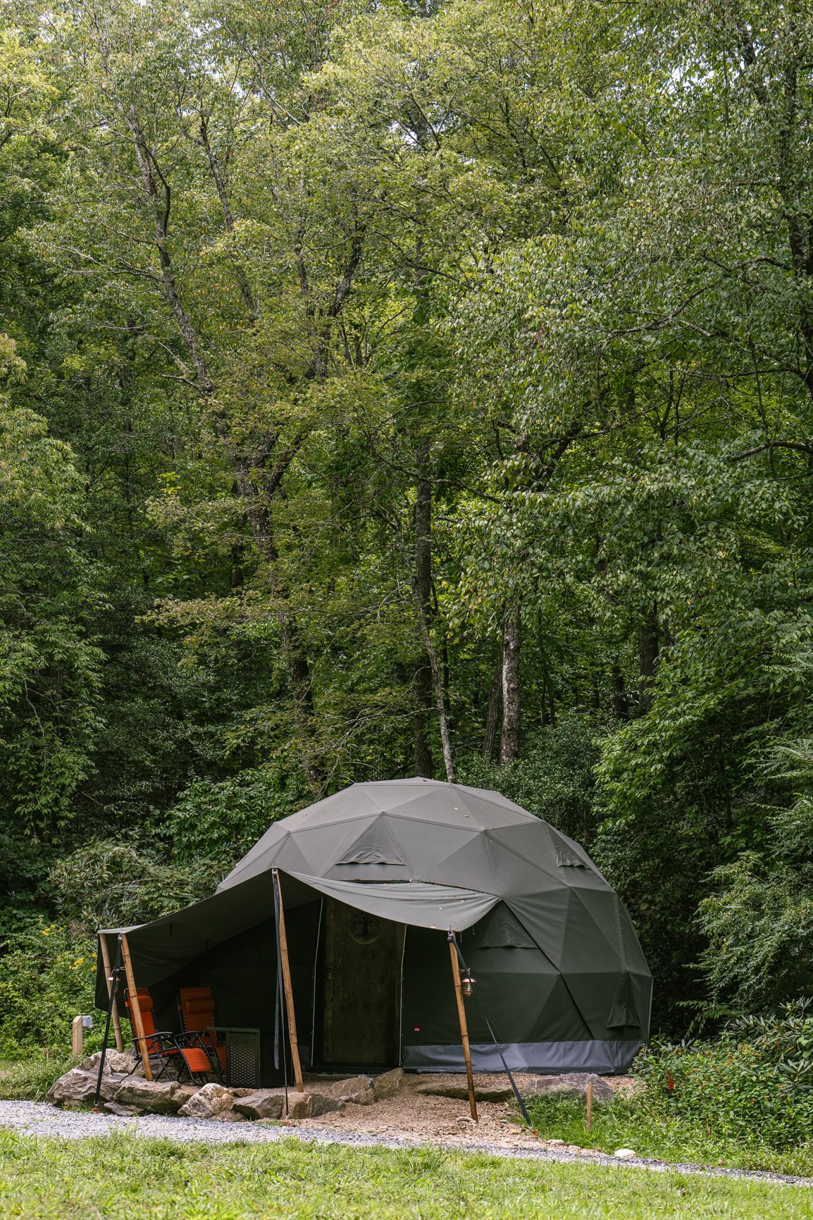 Green dome tent with awning set in a wooded area.