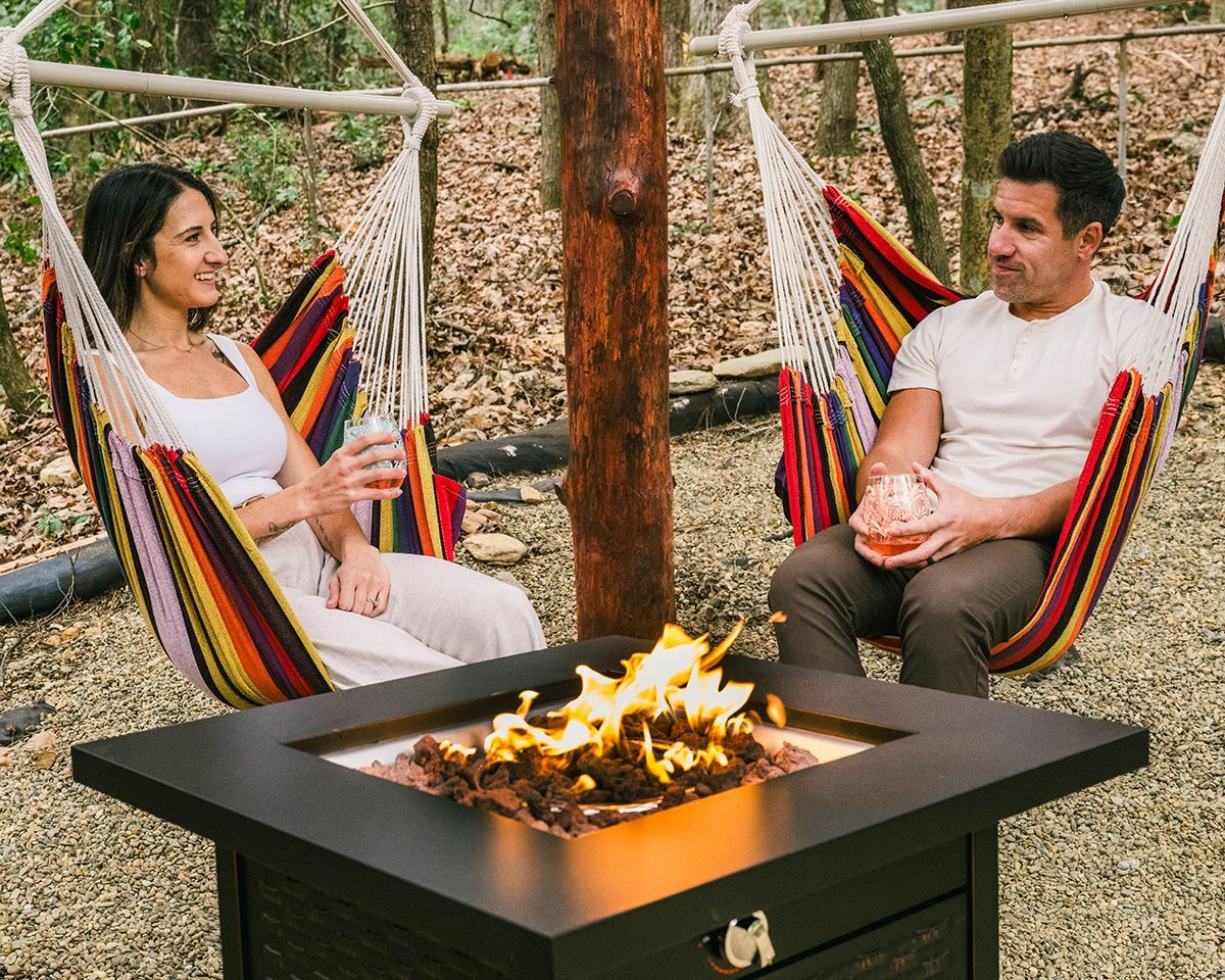 A couple sits by a fire pit with drinks.