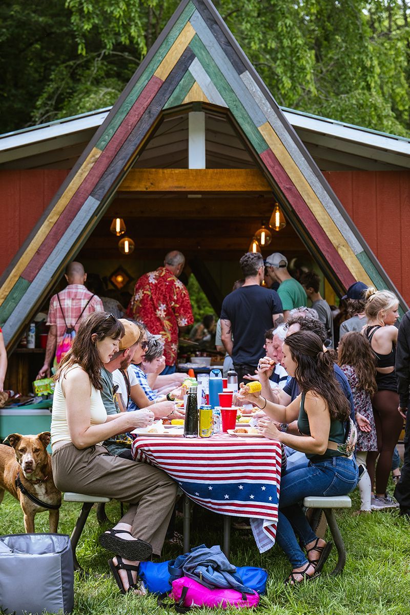 A group of people are eating at a picnic table outside of an outdoor kitchen.