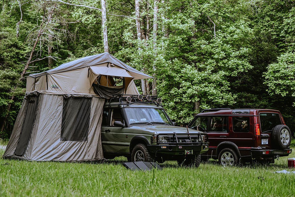 Two Land Rovers with tents sit at a campsite.