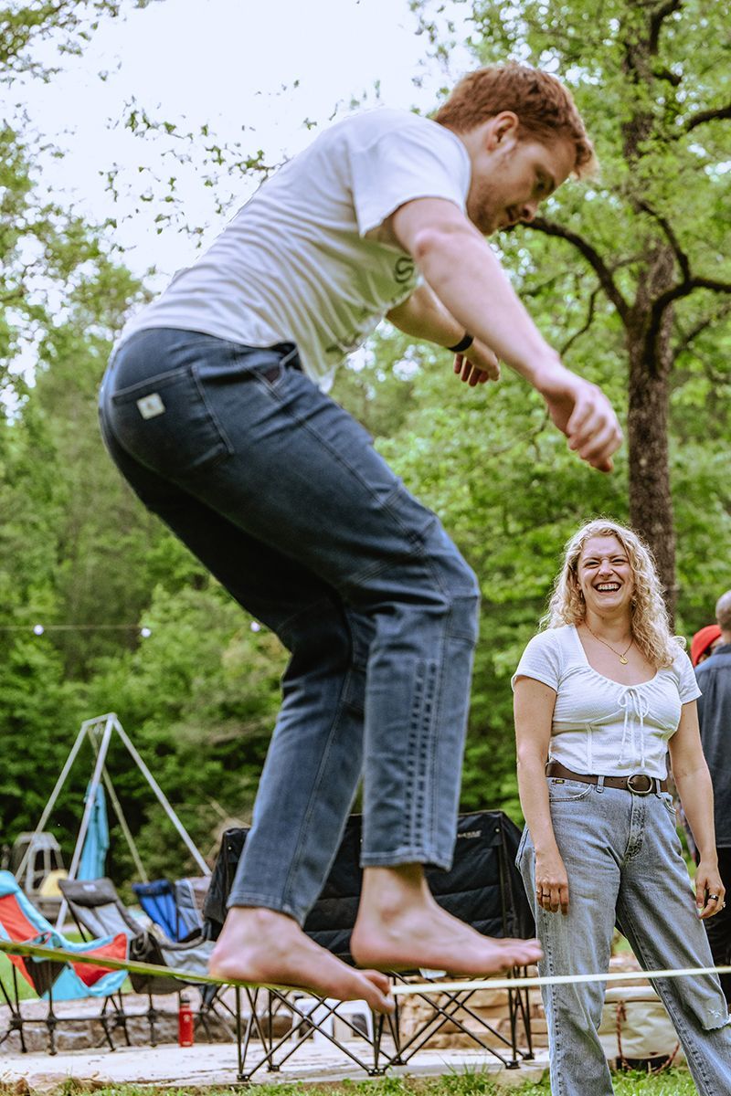 A man balances on a slackline as a woman watches.