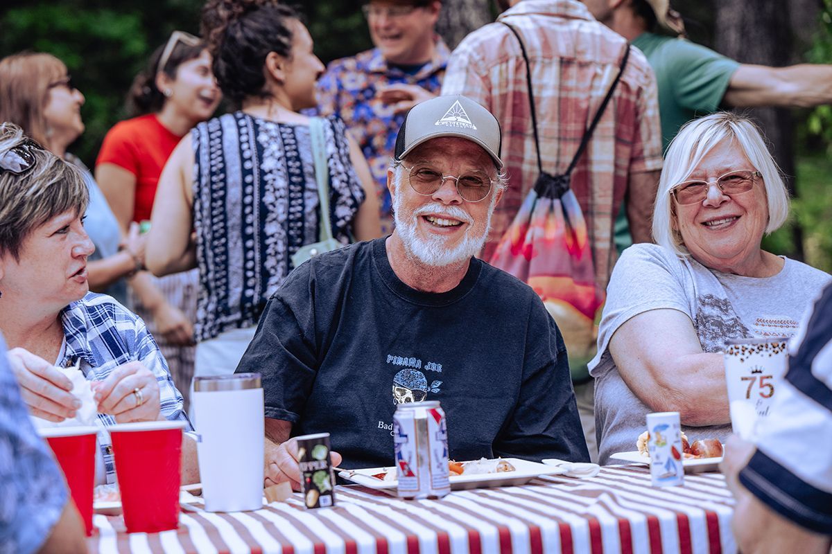 Three women are sitting on a blanket in the woods.