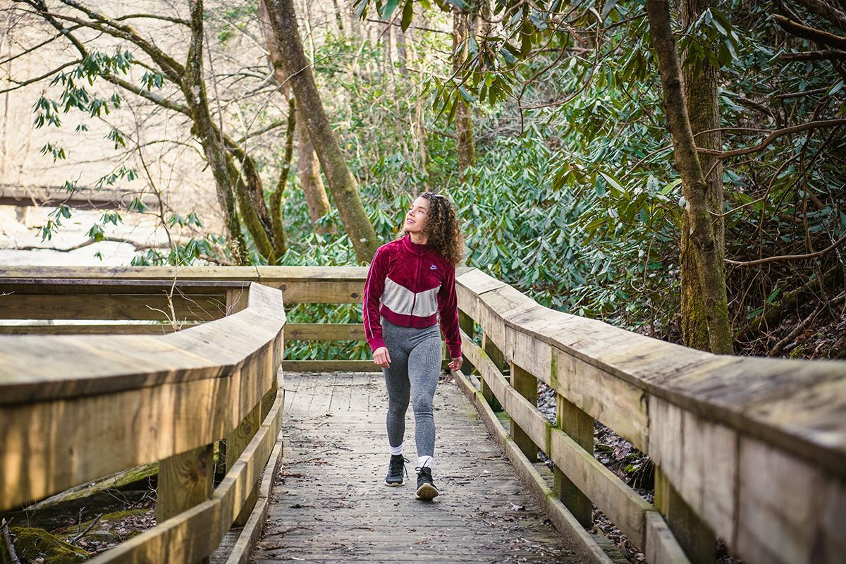 A woman is carrying a child in a backpack on a path in the woods.