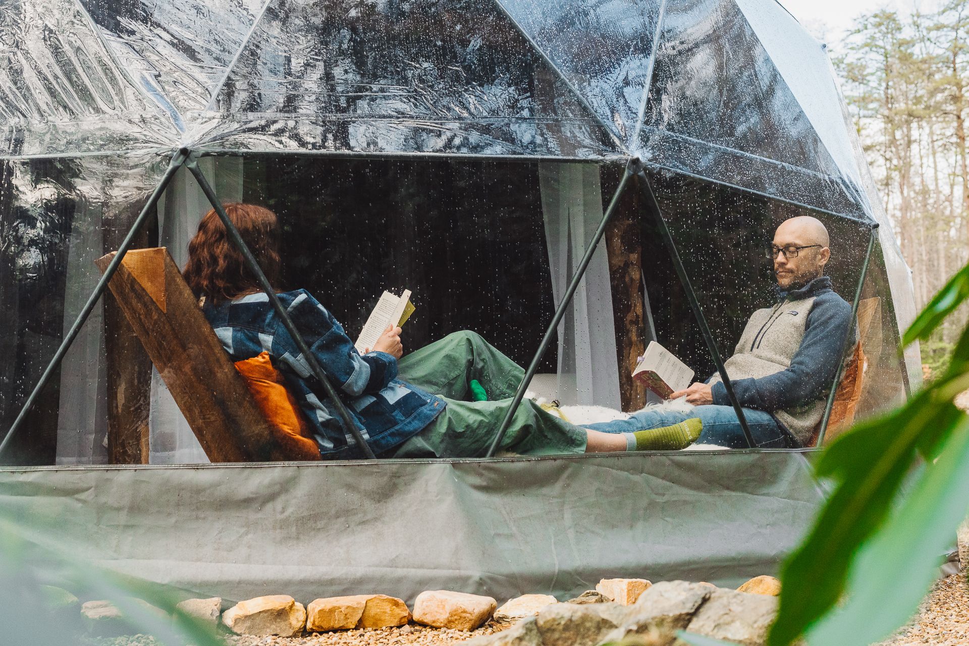 A man and woman read in camping dome