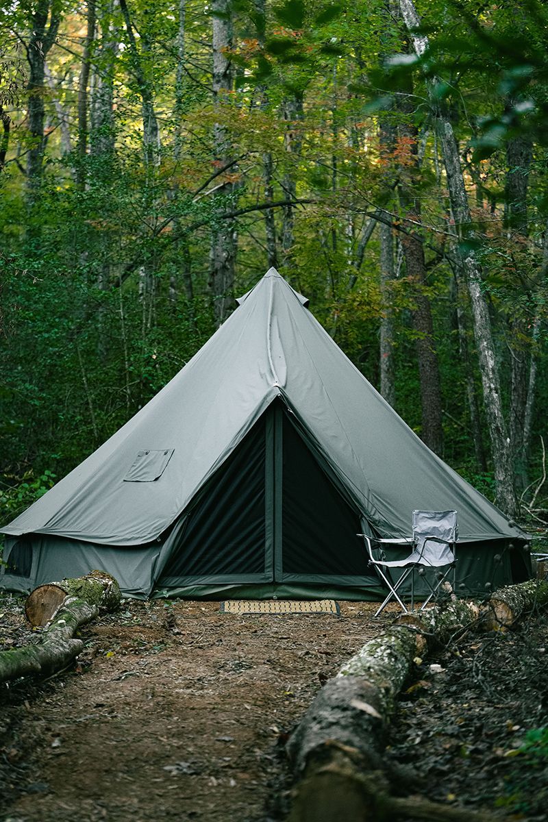 Large canvas tent in a forest setting; a log and camping chair are nearby.