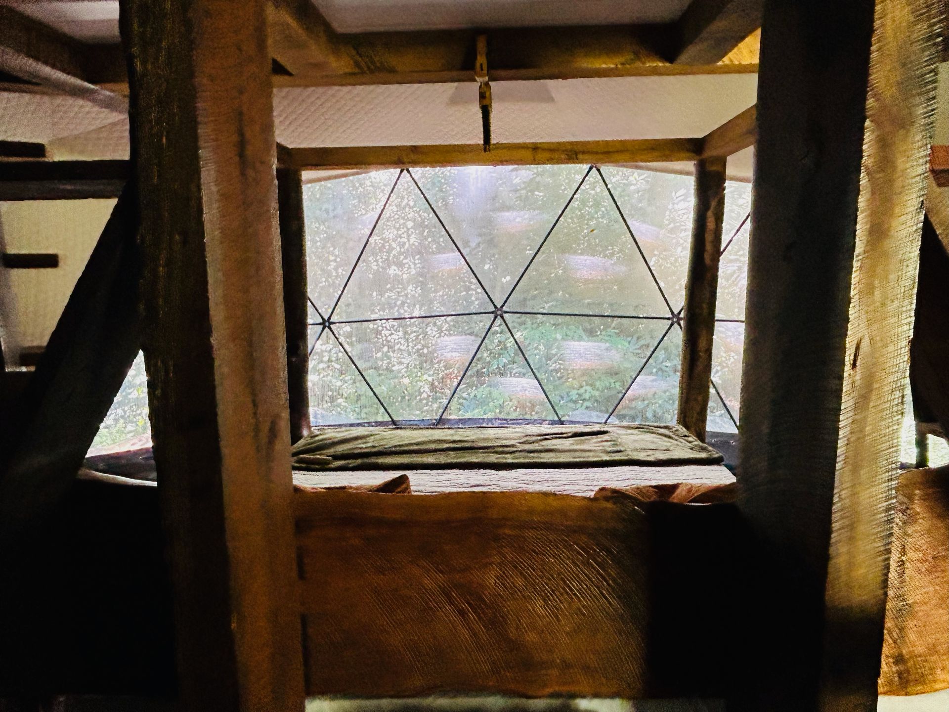 Interior view: wooden beams framing a diamond-paned window. A wooden surface below the window, inside a geodesic down tent. 