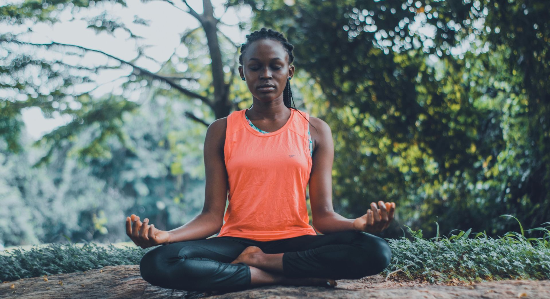 A woman is sitting in a lotus position in a park.
