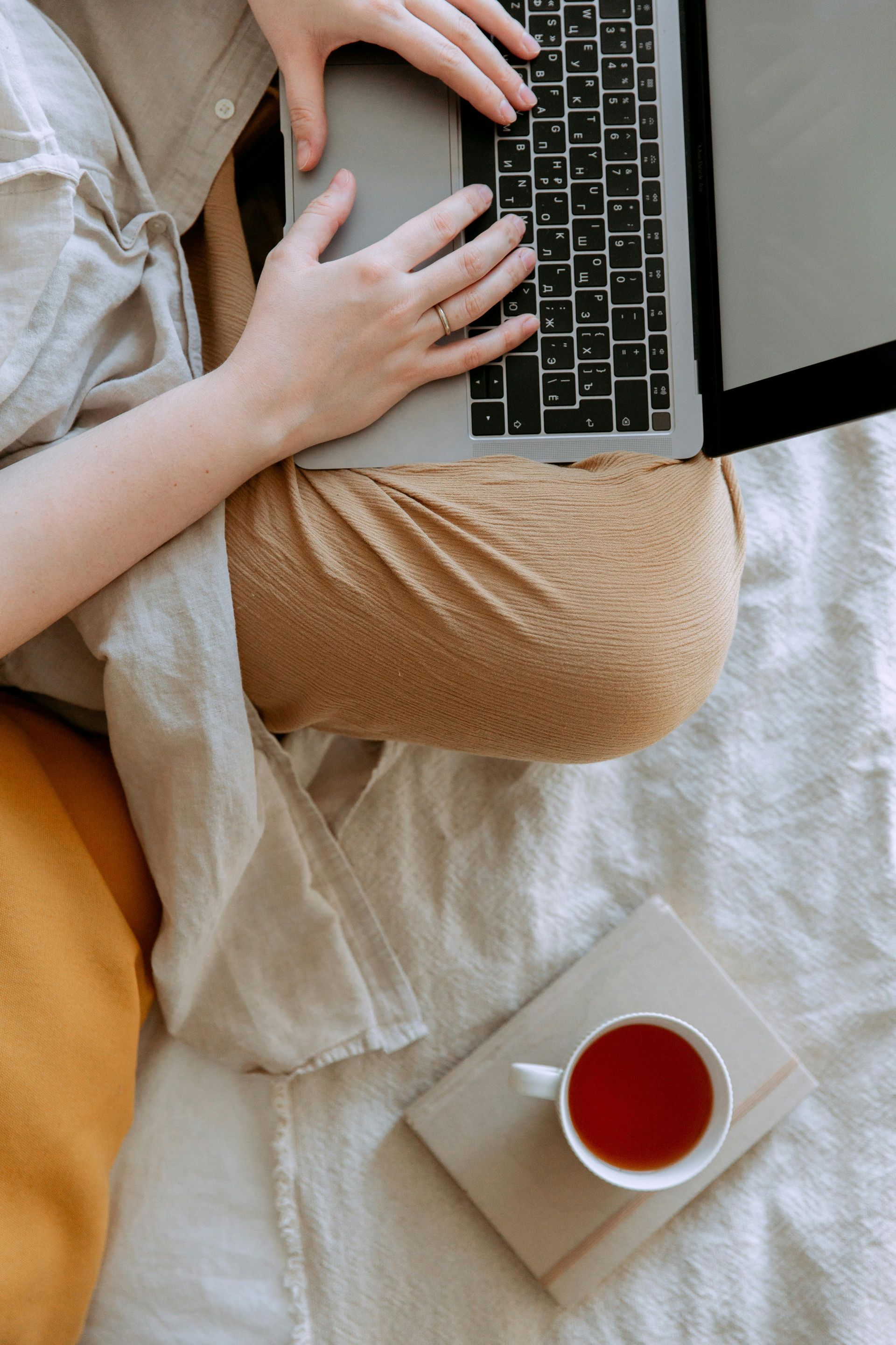 A person is sitting on a bed using a laptop computer.