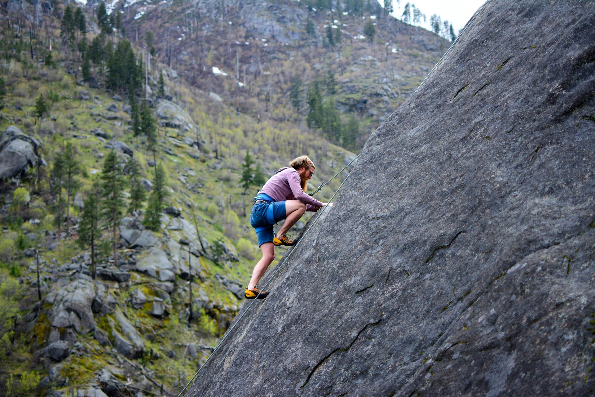 A woman is climbing a rock wall in the mountains.