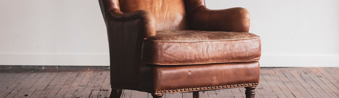 Brown leather armchair on a hardwood floor, against a white wall.