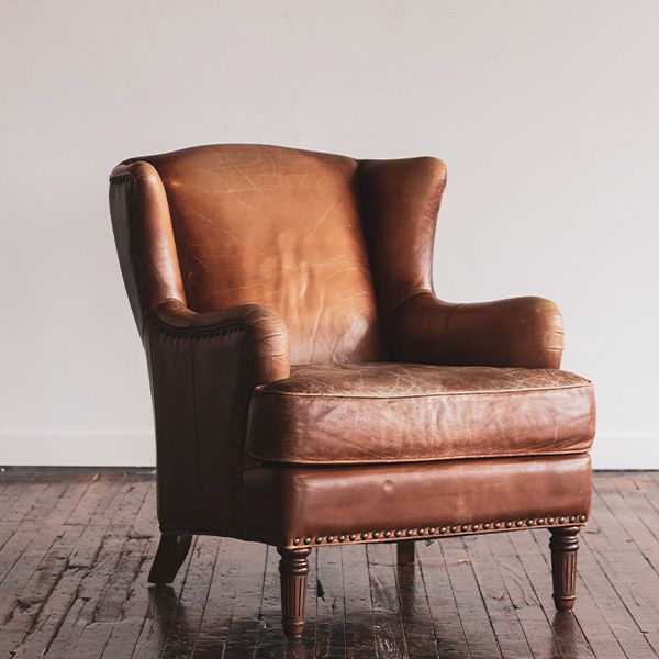 Brown leather armchair in a room with hardwood floors and a white wall.