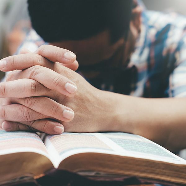 A woman is praying over an open bible with her hands folded