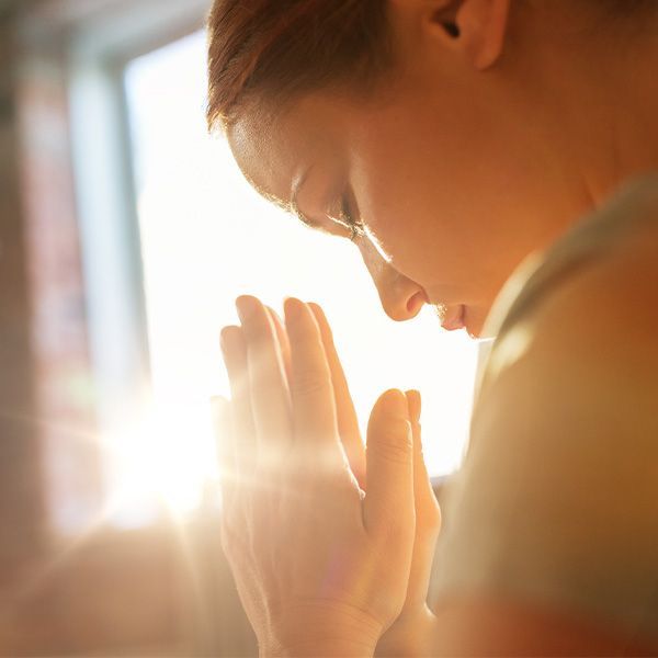 Woman with hands clasped in prayer, bathed in sunlight.