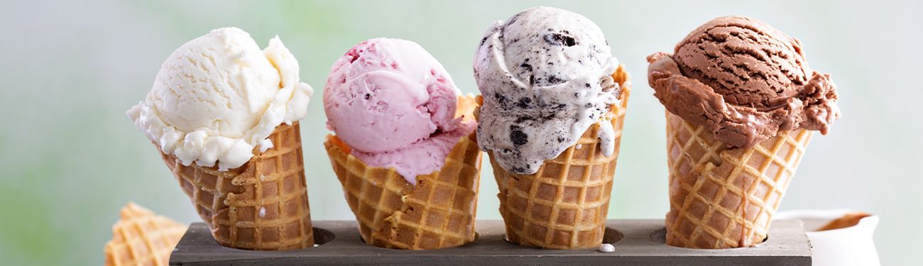 Four ice cream cones with vanilla, strawberry, cookies and cream, and chocolate ice cream.