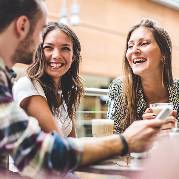 A group of people are sitting at a table laughing and drinking coffee.