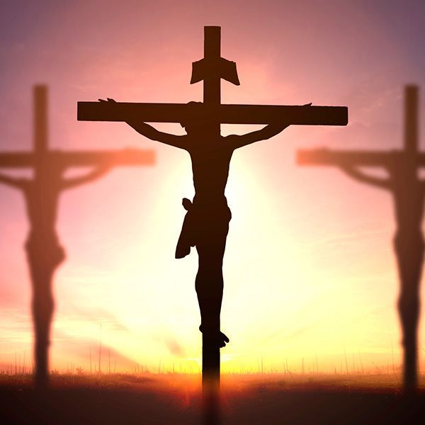 Silhouette of Jesus on a cross, with two other crosses in the background, against a sunset.