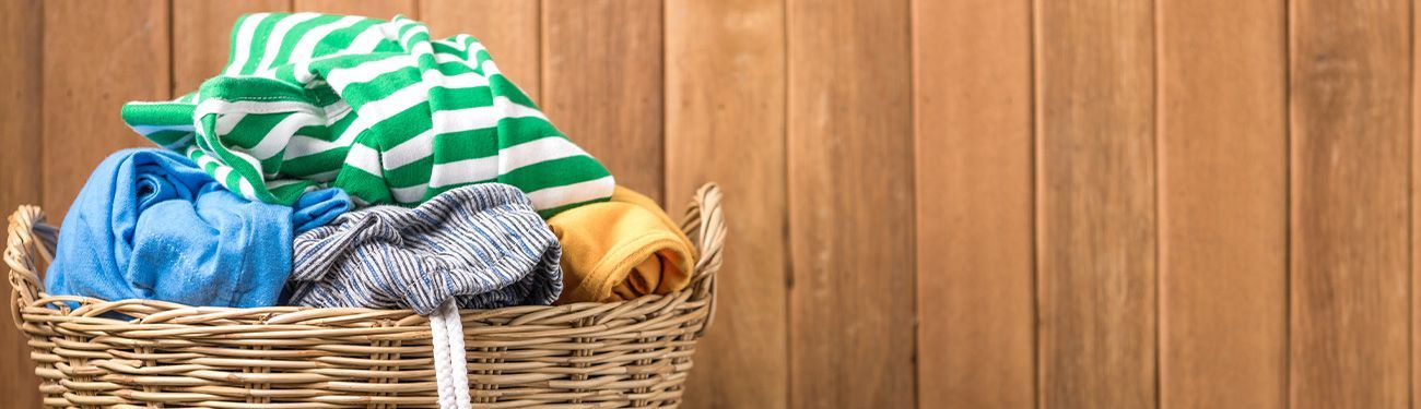 A laundry basket filled with clothes against a wooden wall.