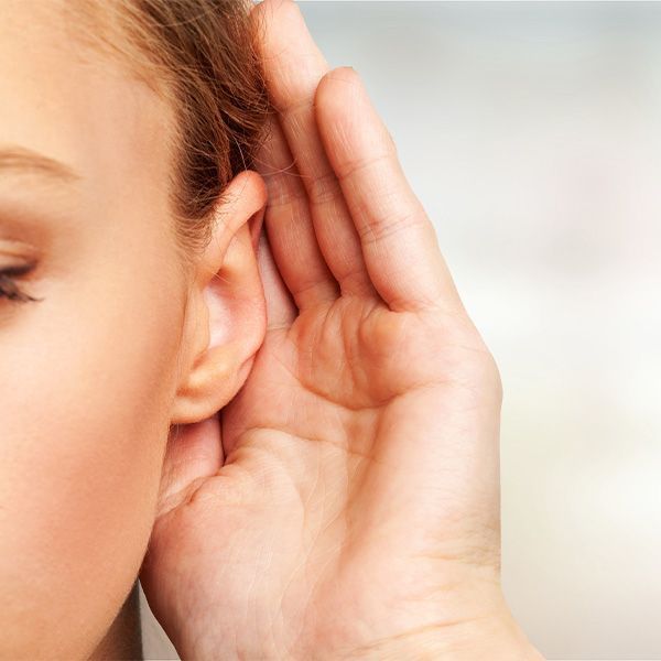A woman is holding her hand to her ear to hear something.