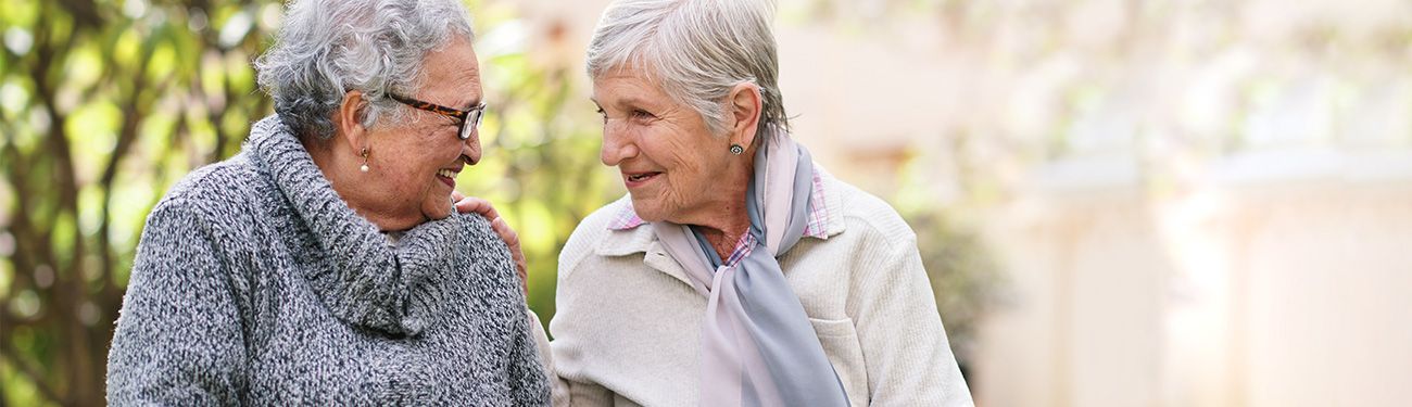 Two elderly women are walking down a path and talking to each other.
