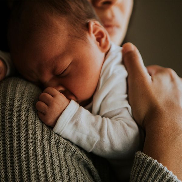 Newborn baby sleeping on a person's shoulder, wearing a white onesie.
