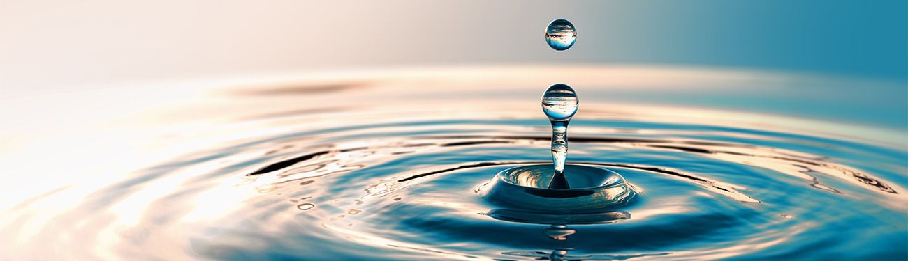 Water drops in mid-air, creating ripples in the water below, with a soft, blurred background.