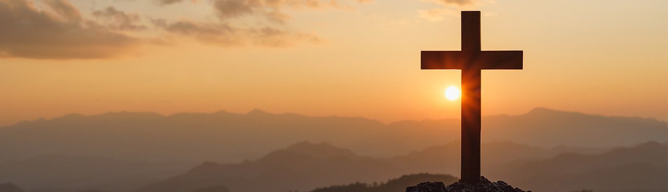 Silhouette of a cross on a mountaintop at sunset, with the sun behind the cross.