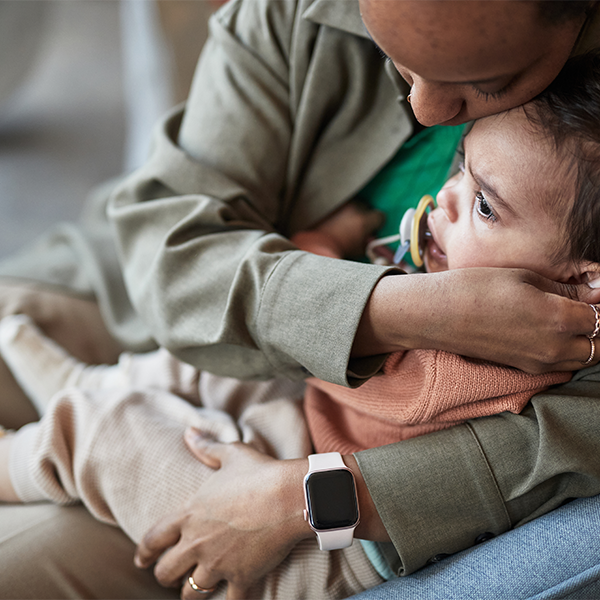 Adult cuddling a child on a couch, both wearing green and beige clothing, with a smartwatch visible.