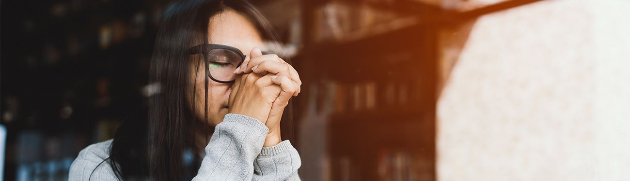 A woman wearing glasses is covering her face with her hands.