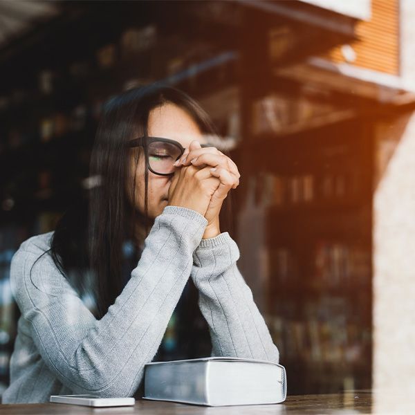 A woman is sitting at a table with her hands folded in prayer.