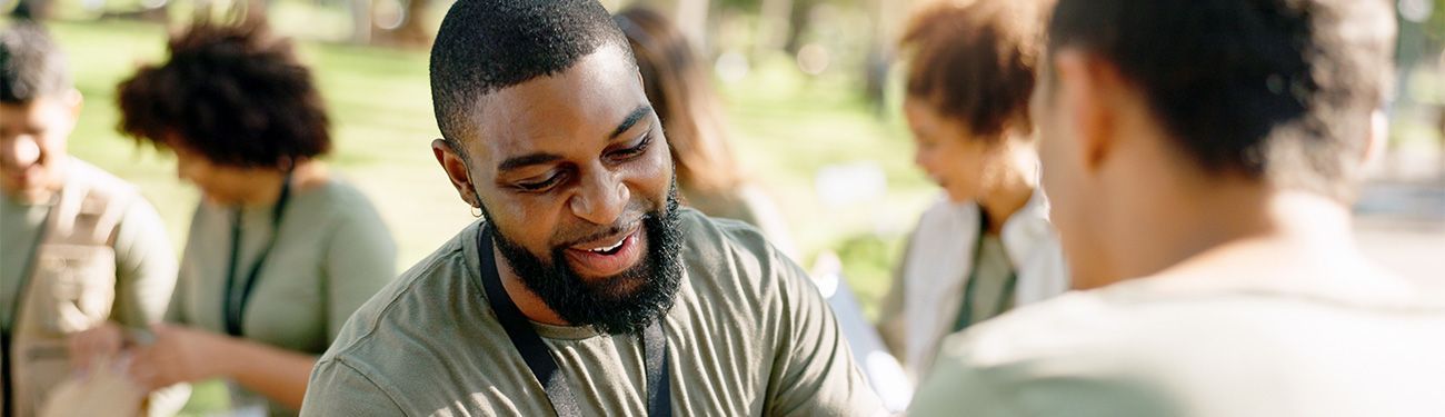 A man with a beard is talking to a woman in a park as they volunteer.
