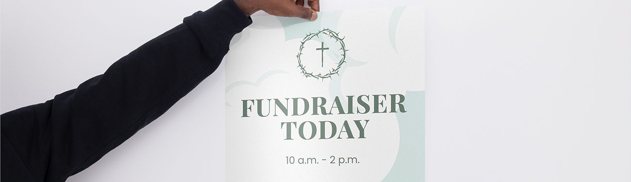 Hand holding a white sign with “FUNDRAISER TODAY” and a cross on it. 