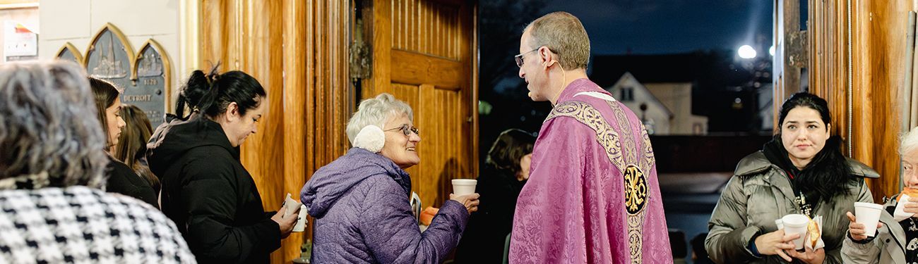 People are gathered near a parish door, some holding cups.