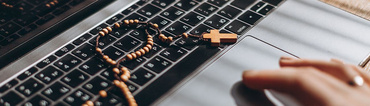 Computer keyboard with a rosary on top of it. 
