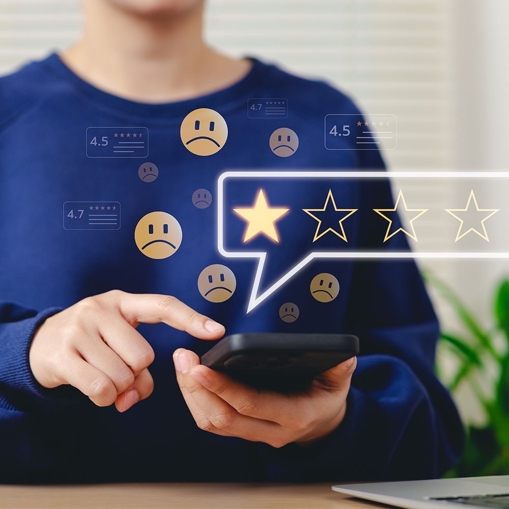 A person in a blue sweater is holding a cell phone creating a one star review.