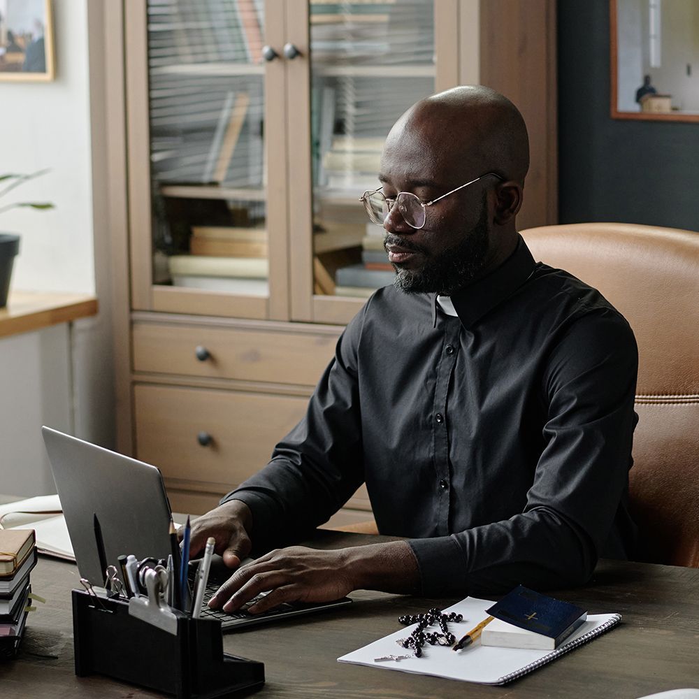 Catholic priest typing on a laptop in an office